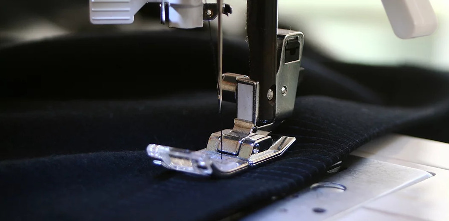 Close-up of a sewing machine needle stitching dark fabric during industrial sewing work.